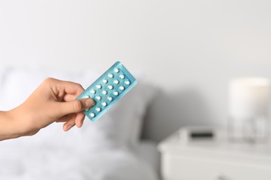 Photo of Woman holding blister of oral contraception pills against blurred background, closeup. Space for text