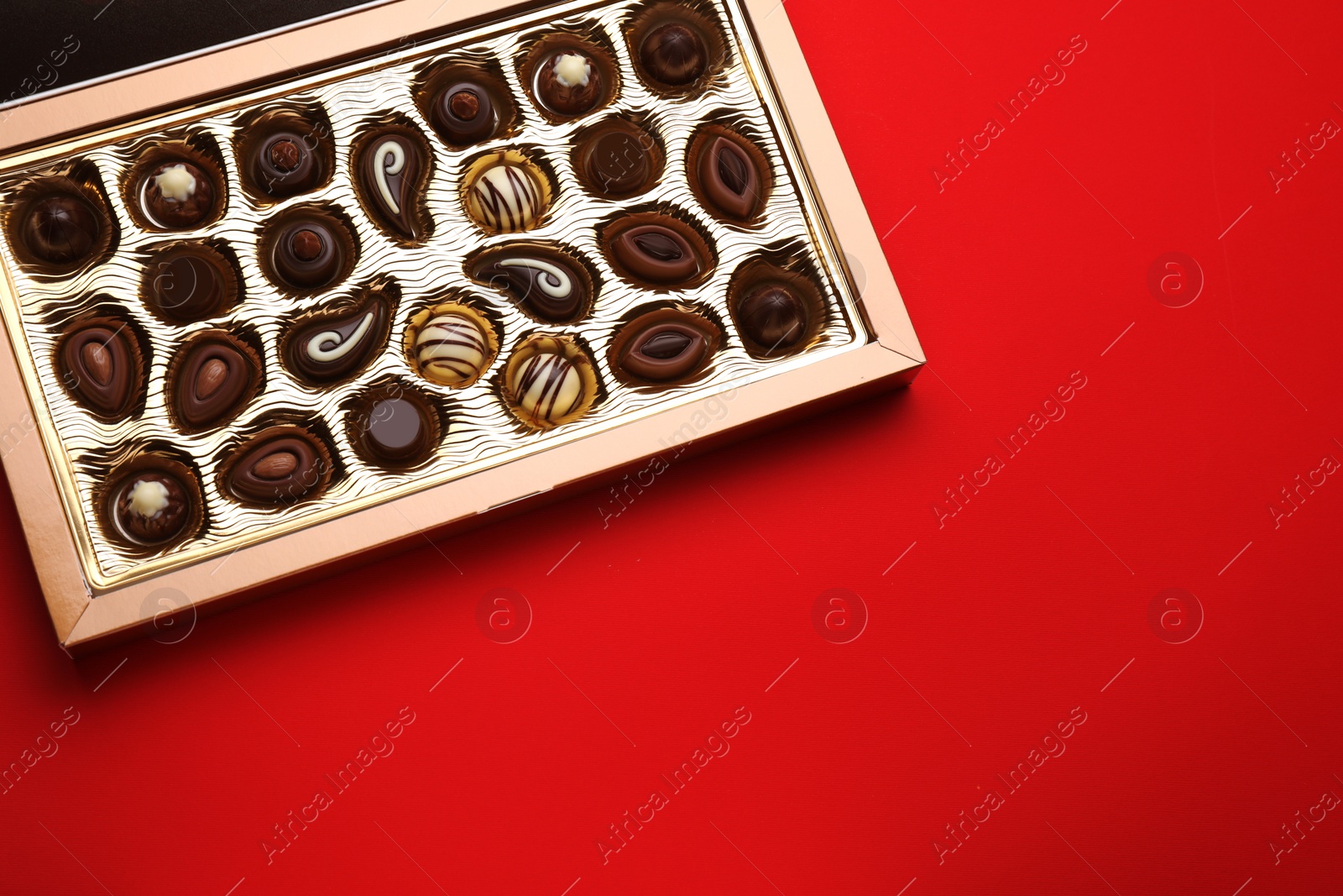 Photo of Box of delicious chocolate candies on red background, top view. Space for text