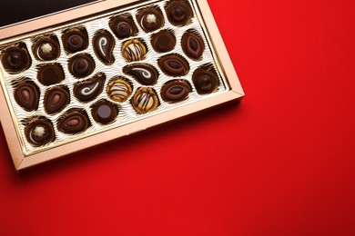 Photo of Box of delicious chocolate candies on red background, top view. Space for text