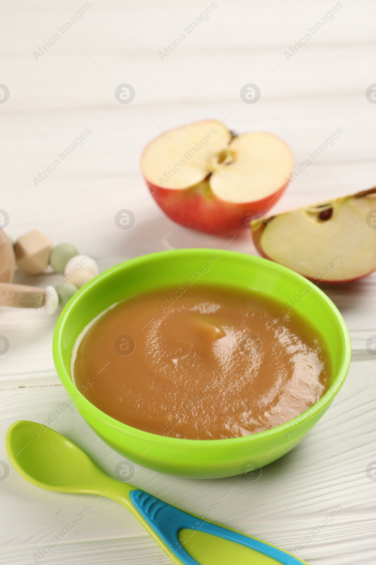 Photo of Baby food. Puree of apples in bowl and spoon on white wooden table