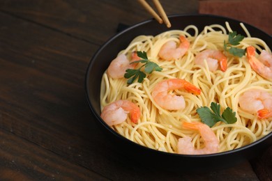 Photo of Tasty spaghetti with shrimps and parsley in bowl on wooden table, closeup. Space for text