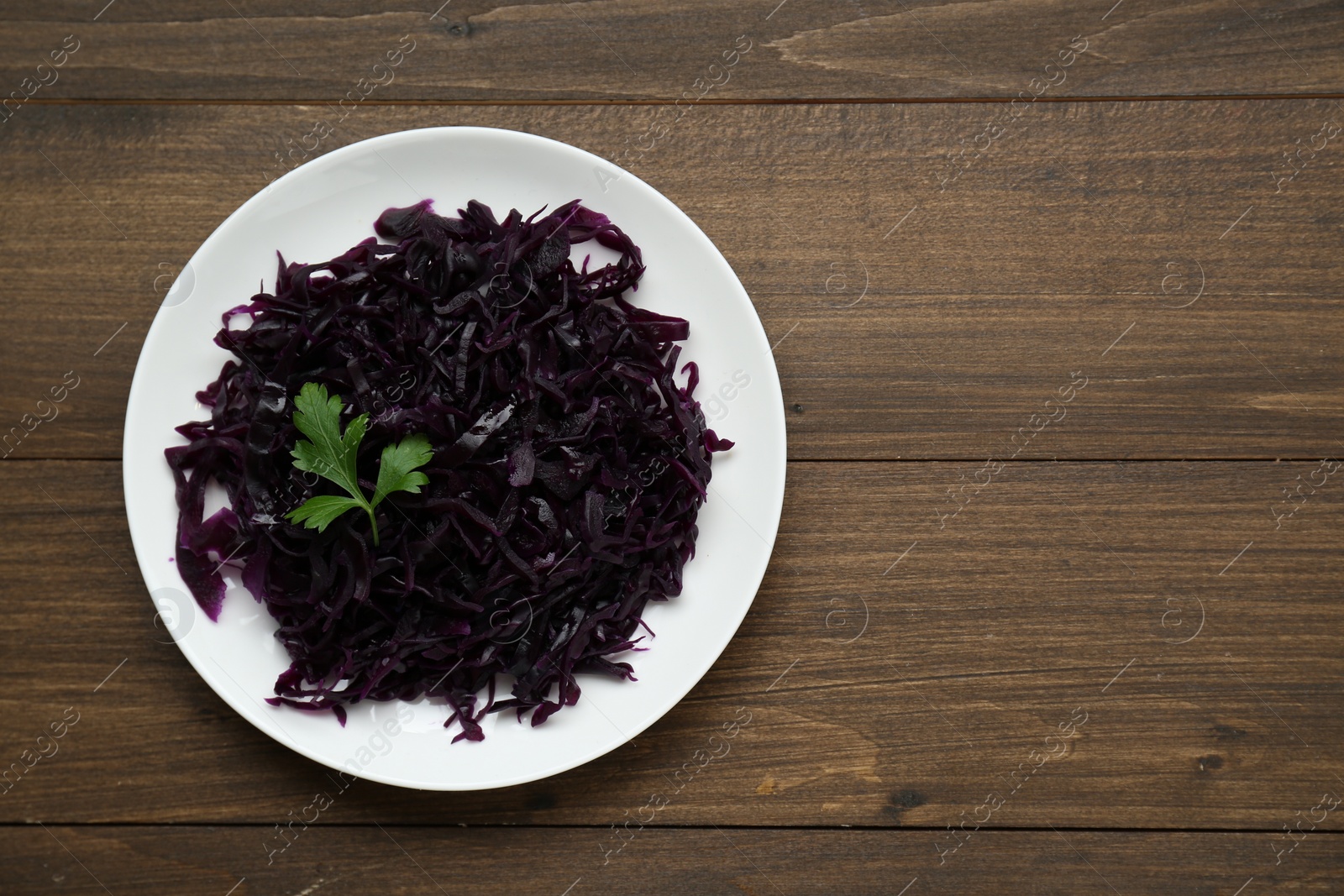 Photo of Tasty red cabbage sauerkraut with parsley on wooden table, top view. Space for text