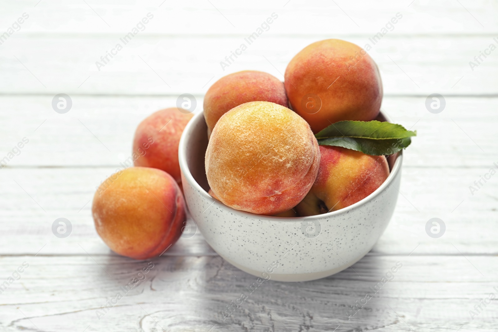 Photo of Bowl with delicious ripe peaches on wooden background