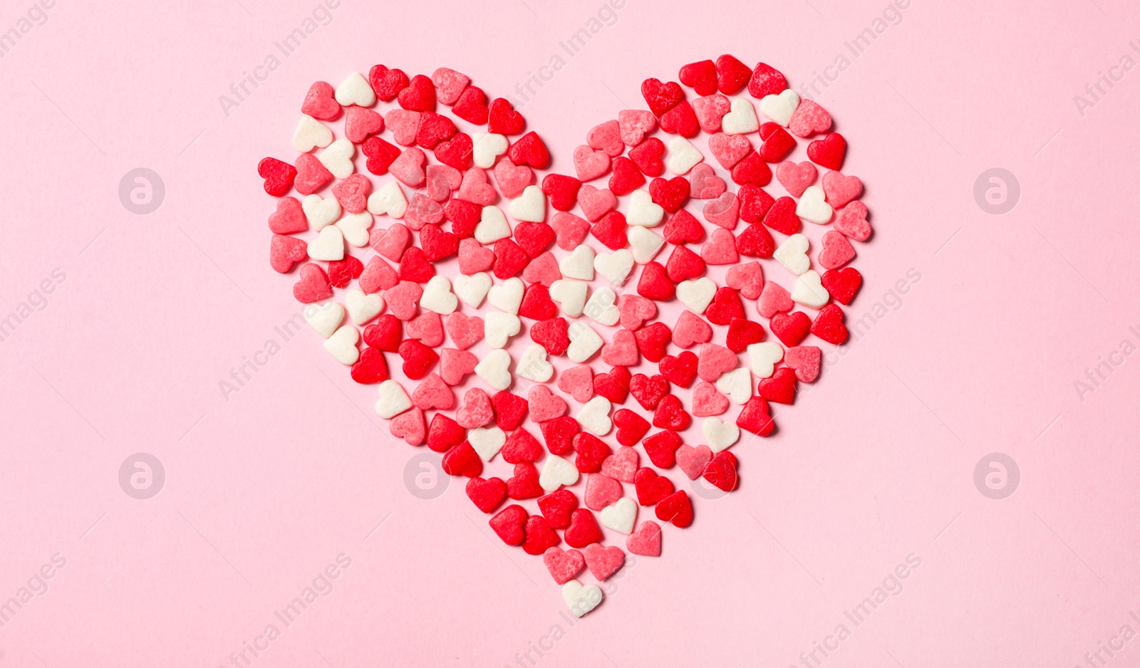 Photo of Heart made with sprinkles on pink background, top view