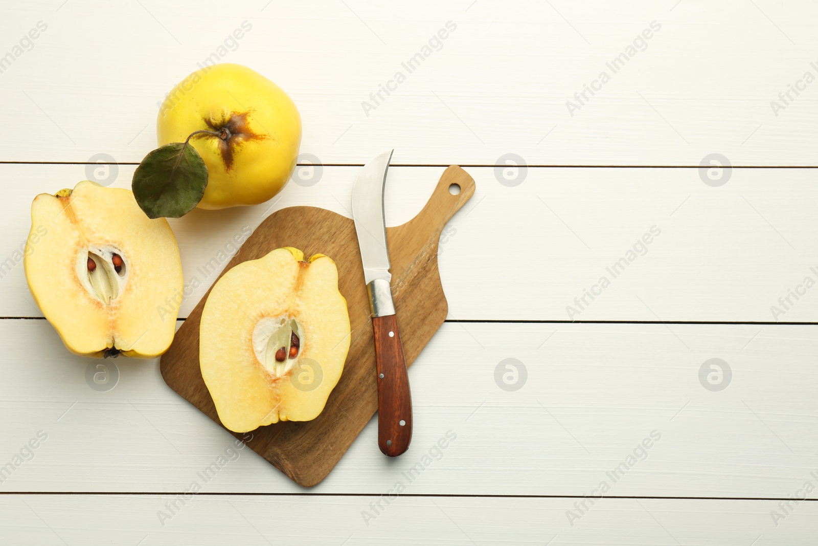 Photo of Tasty ripe quince fruits and knife on white wooden table, flat lay. Space for text