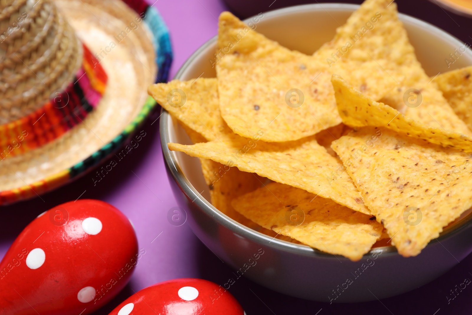 Photo of Nachos chips, maracas and Mexican sombrero hat on purple background, closeup