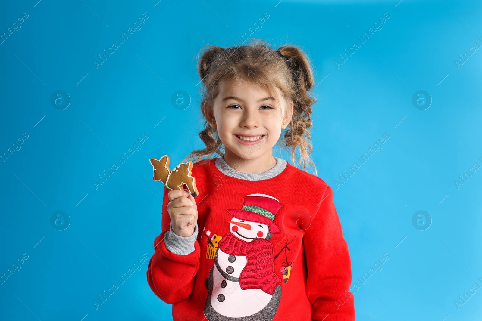 Photo of Cute little girl with Christmas gingerbread cookie on light blue background