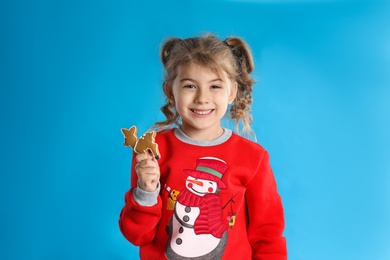 Photo of Cute little girl with Christmas gingerbread cookie on light blue background