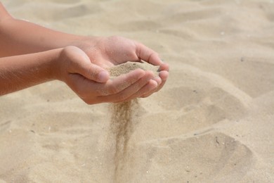 Child pouring sand from hands on beach, closeup with space for text. Fleeting time concept