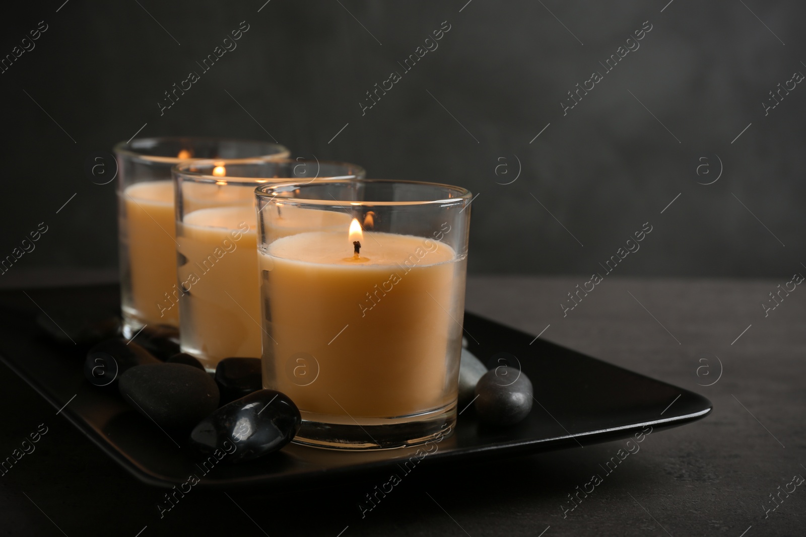 Photo of Dark plate with three burning candles and rocks on table, space for text