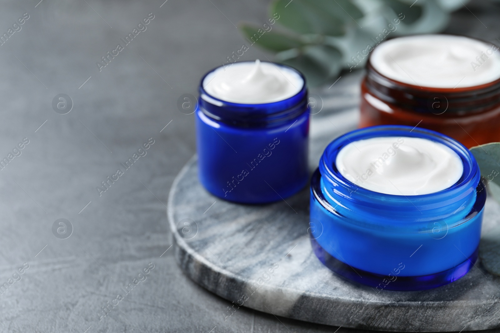 Photo of Jars of organic cream on dark grey stone table. Space for text