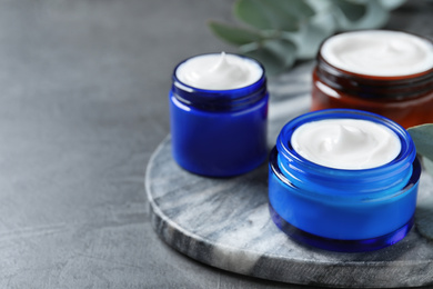 Jars of organic cream on dark grey stone table. Space for text