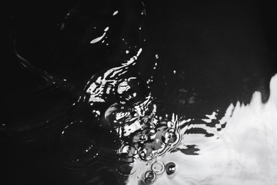 Photo of Rain drops falling down into puddle on dark background, above view