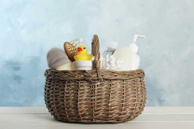 Photo of Wicker basket full of different baby cosmetic products, accessories and toy on white wooden table
