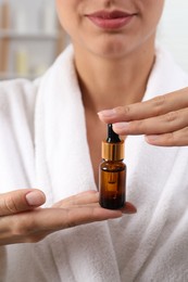 Woman with bottle of cosmetic serum on blurred background, closeup