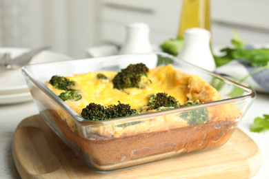Photo of Tasty broccoli casserole in baking dish on wooden board, closeup