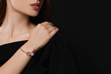 Young woman wearing elegant pearl bracelet on black background, closeup. Space for text