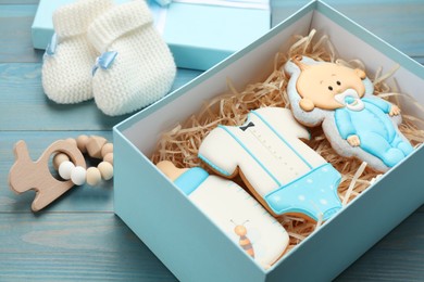 Photo of Set of baby shower cookies in gift box and accessories on turquoise wooden table, closeup