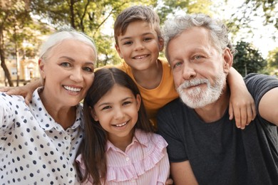 Photo of Happy grandparents with little children taking selfie in park