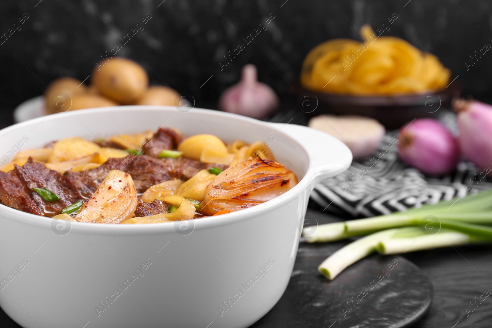 Photo of Pot of delicious vegetable soup with meat, noodles and ingredients on black wooden table, closeup. Space for text