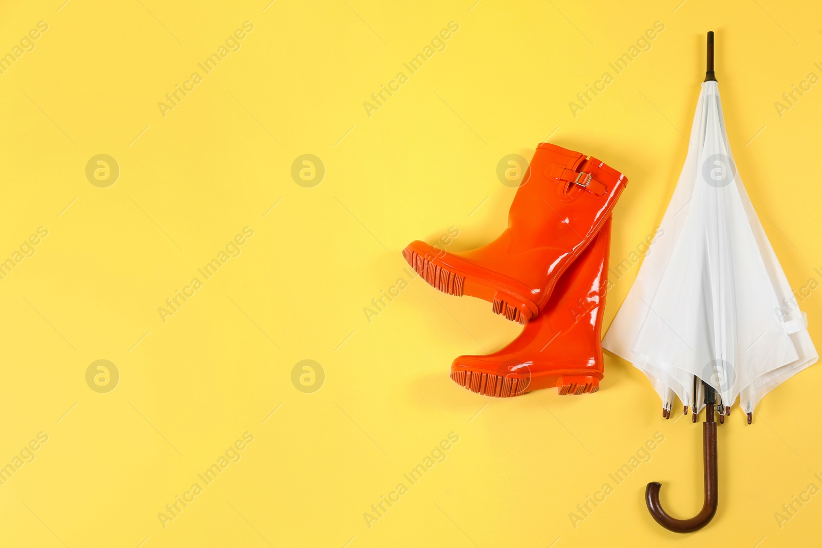 Photo of Beautiful white umbrella and red rubber boots on light yellow background, flat lay. Space for text