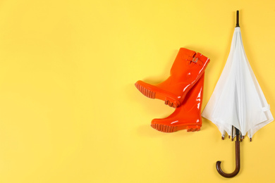 Photo of Beautiful white umbrella and red rubber boots on light yellow background, flat lay. Space for text