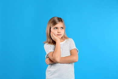 Photo of Thoughtful little girl on light blue background
