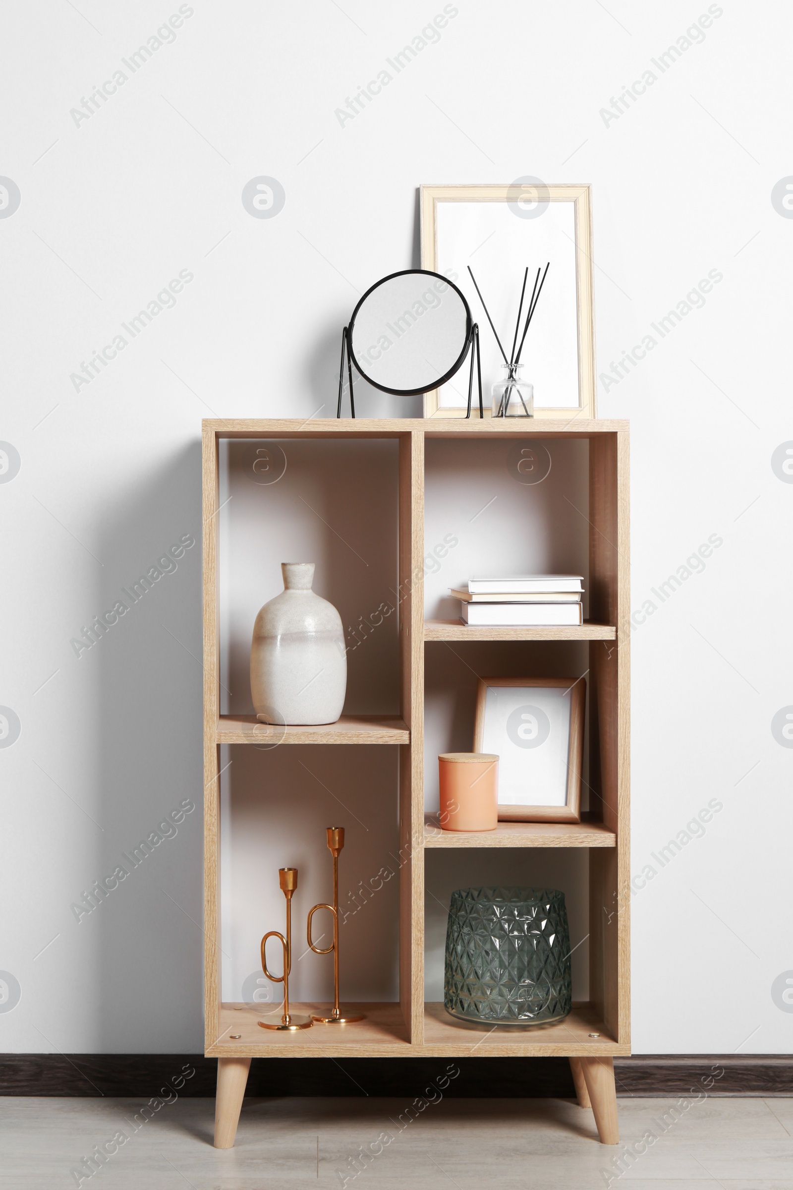 Photo of Stylish mirror, reed diffuser and picture frame on shelf near light wall. Interior design