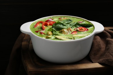 Photo of Saucepan with delicious green curry chicken soup on wooden board