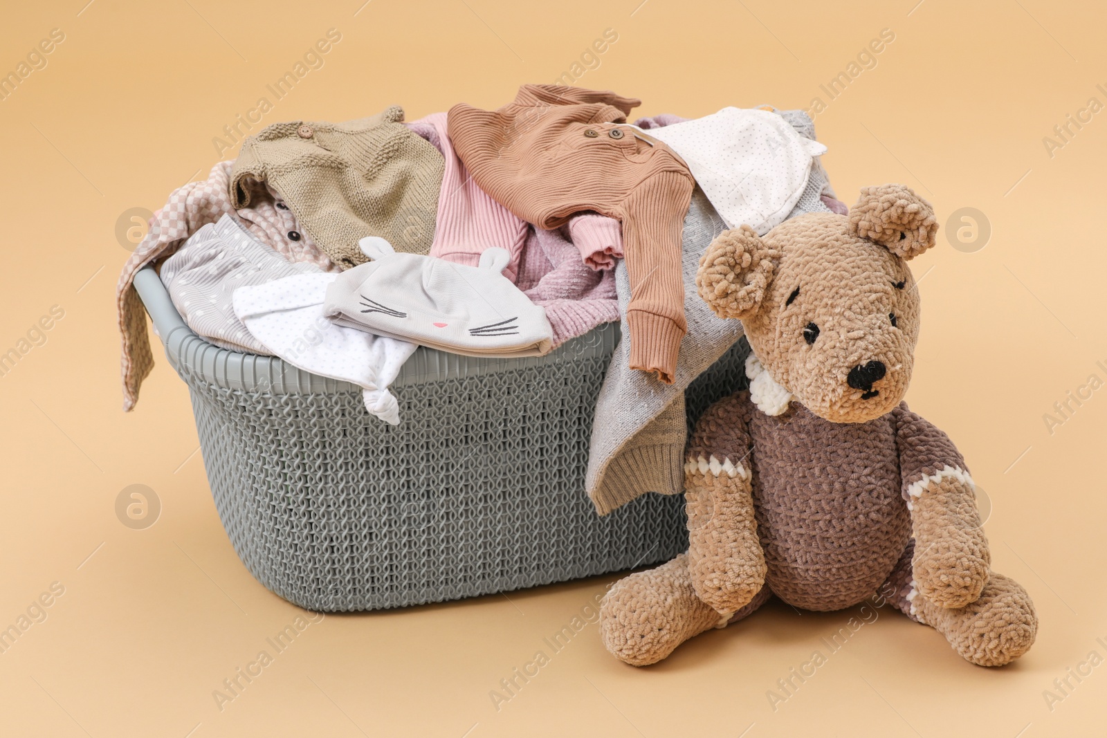 Photo of Laundry basket with baby clothes near soft toy on light brown background