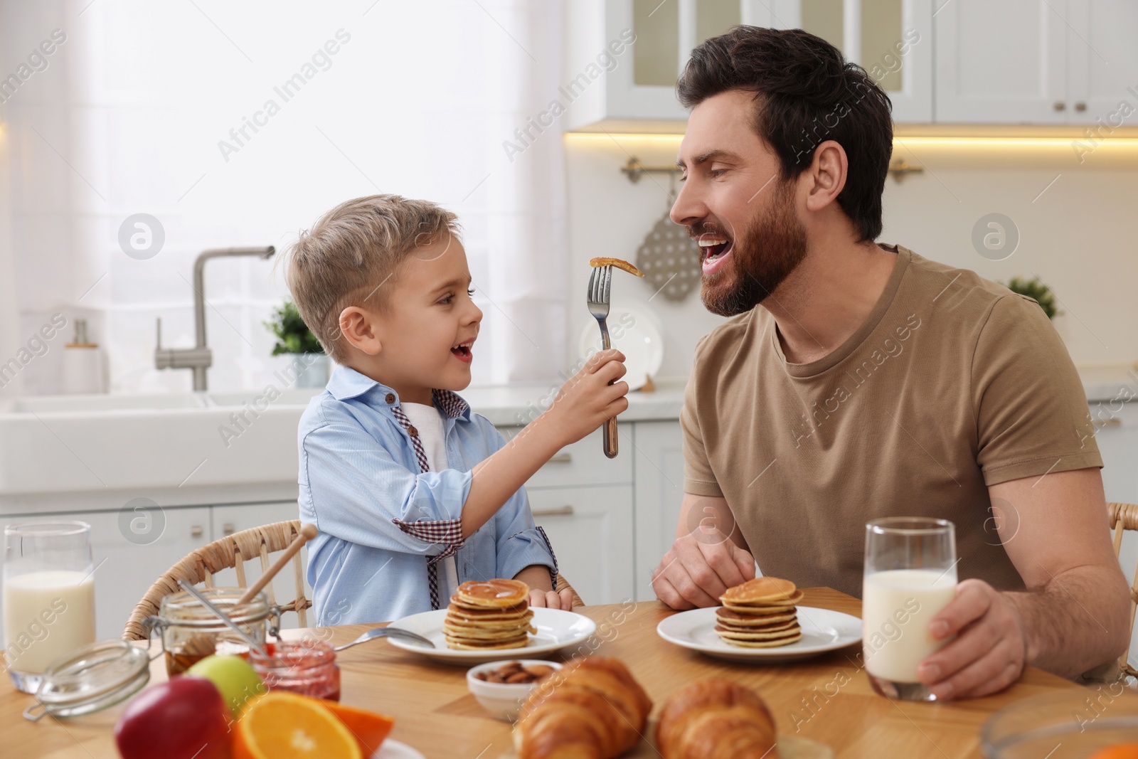 Photo of Father and his cute little son having breakfast at table in kitchen