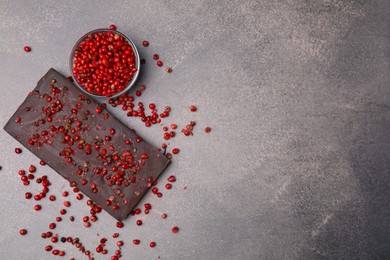 Photo of Delicious chocolate bar and red peppercorns on grey textured table, flat lay. Space for text