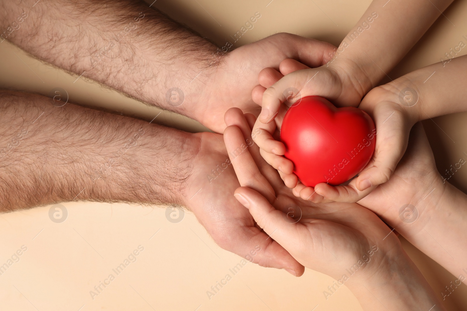 Photo of Parents and kid holding red heart in hands on beige background, top view