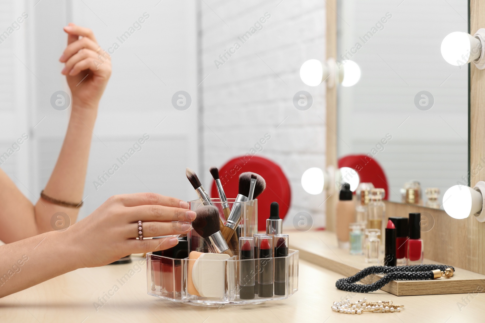 Photo of Woman reaching for organizer with cosmetic products and makeup accessories on dressing table indoors, closeup