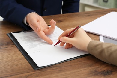 Man pointing at document and woman putting signature at wooden table, closeup