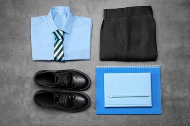 Photo of Stylish school uniform for boy and stationery on grey background, flat lay