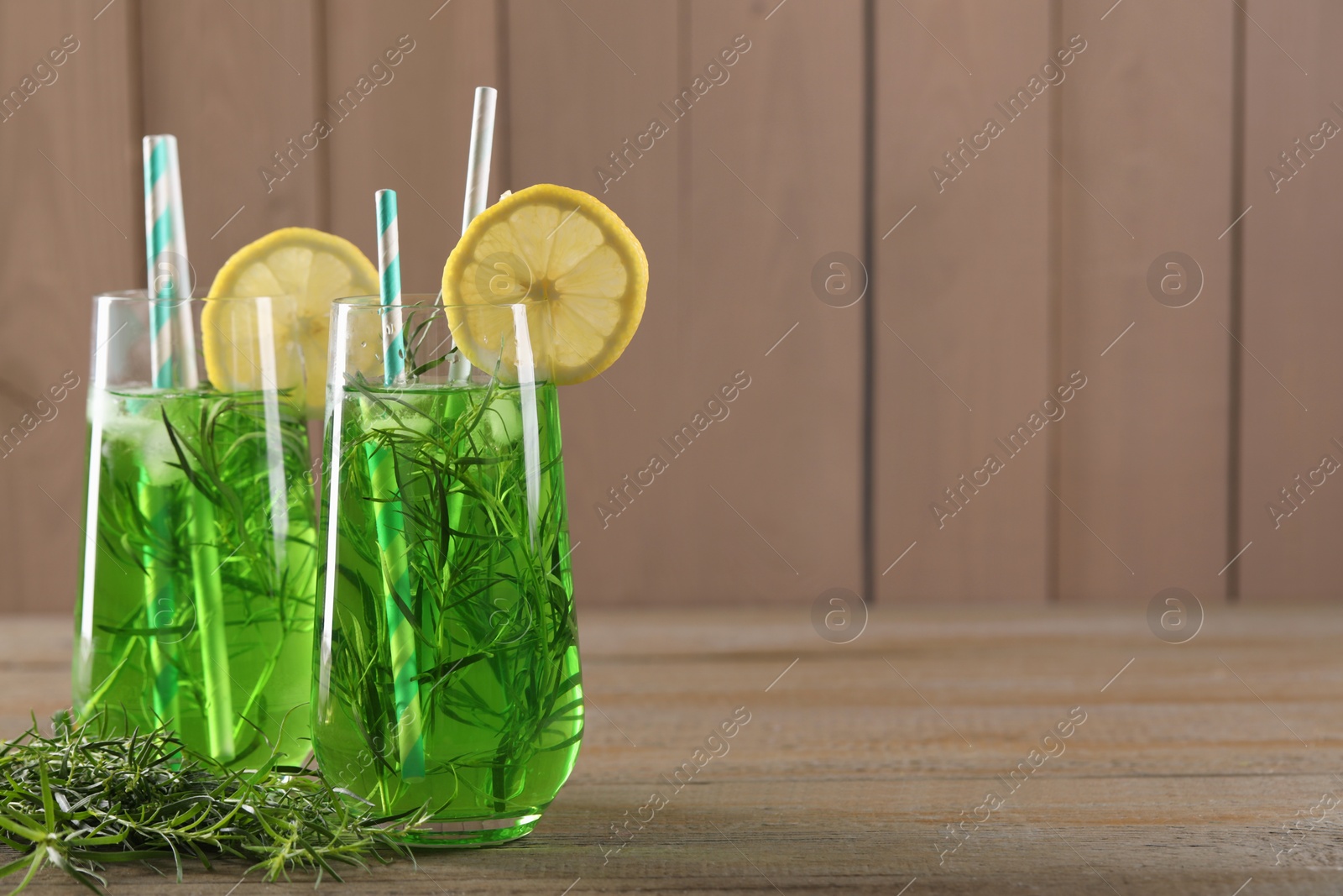 Photo of Glasses of refreshing tarragon drink with lemon slices on wooden table, space for text
