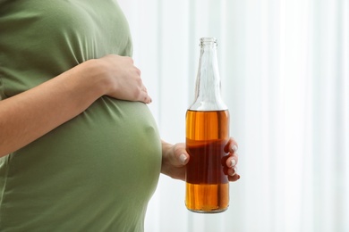 Photo of Pregnant woman with bottle of beer indoors, closeup. Alcohol abuse during pregnancy