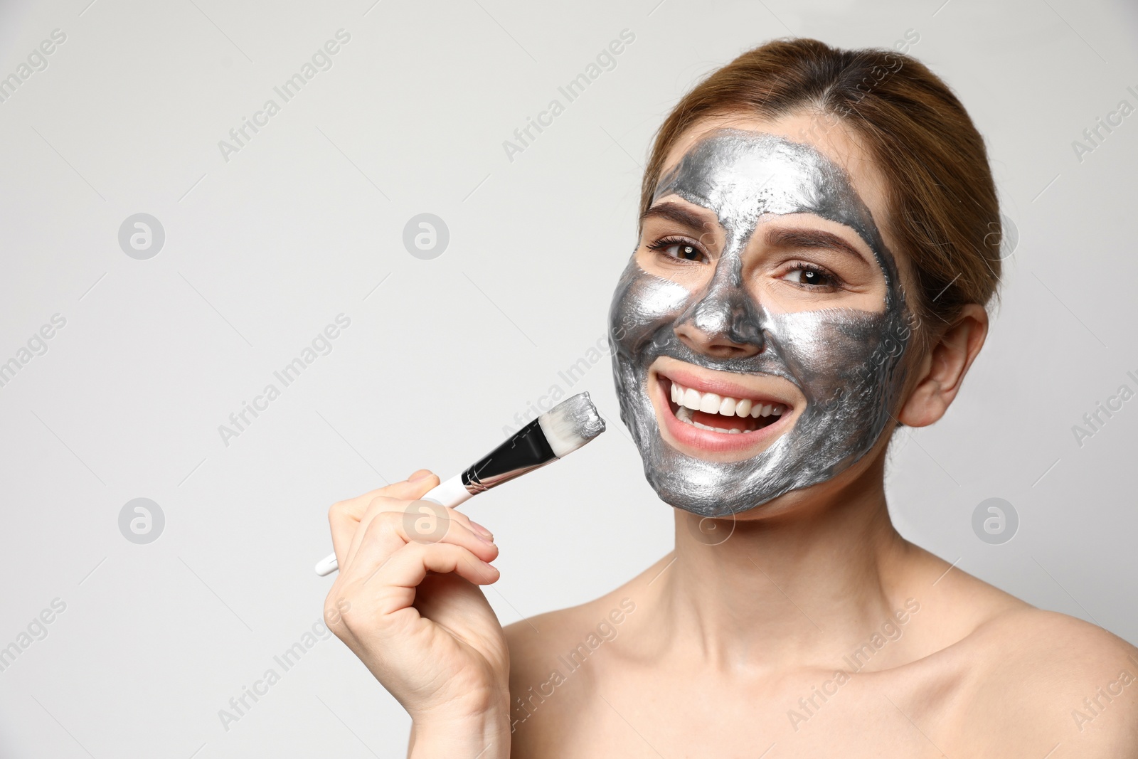 Photo of Beautiful woman applying mask onto face against light background. Space for text