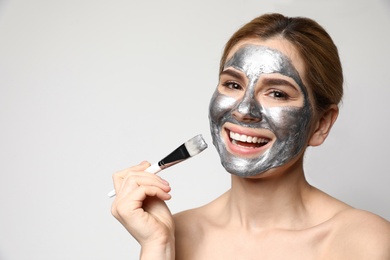 Beautiful woman applying mask onto face against light background. Space for text