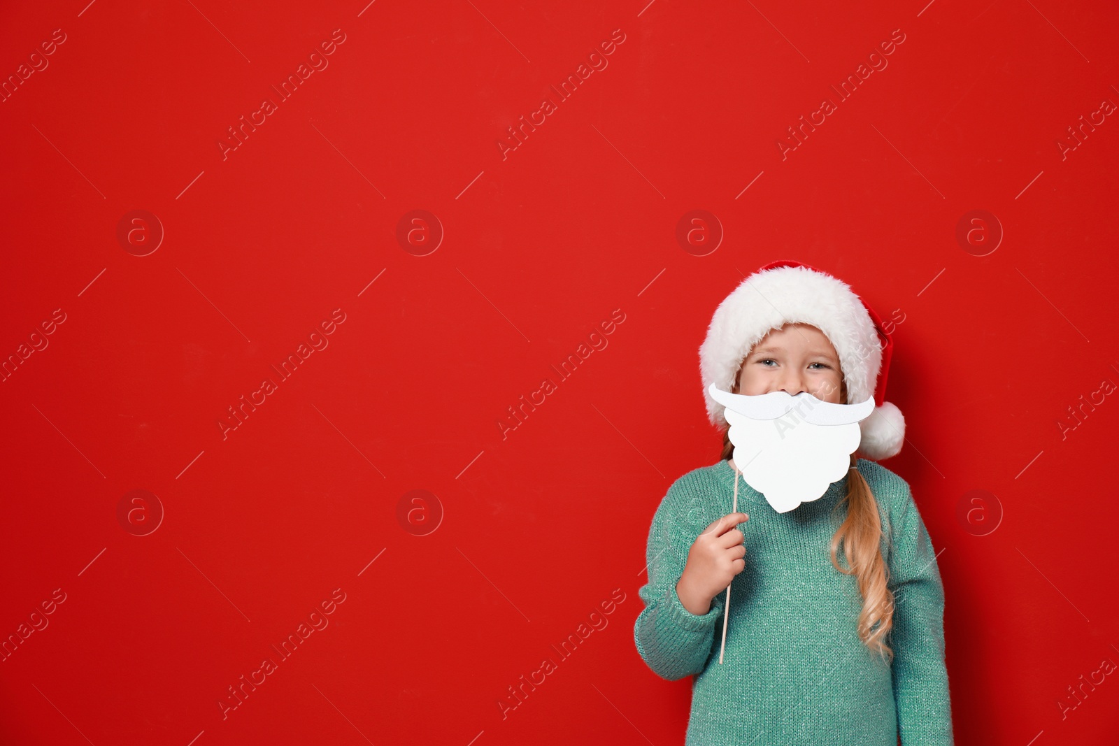 Image of Cute little girl with Santa hat and white beard prop on red background, space for text. Christmas celebration