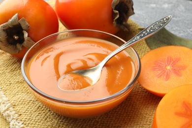 Photo of Delicious persimmon jam in glass bowl served on table, closeup