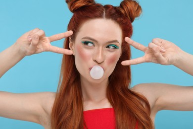 Photo of Portrait of beautiful woman with bright makeup blowing bubble gum and gesturing on light blue background
