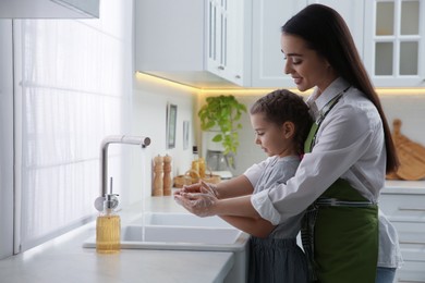 Photo of Mother and daughter washing hands with liquid soap together in kitchen