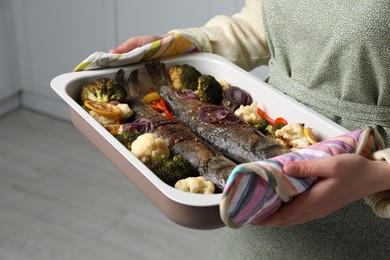 Photo of Woman holding baking tray with sea bass fish and vegetables, closeup