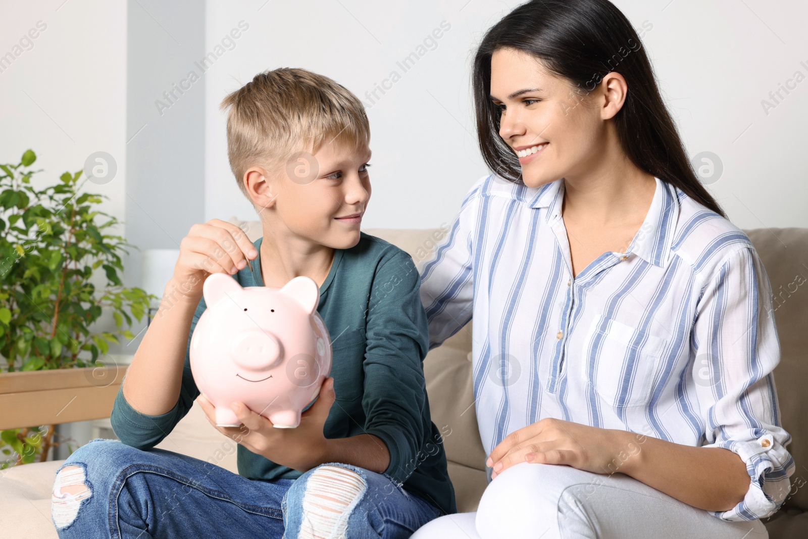 Photo of Boy with his mother putting coin into piggy bank at home