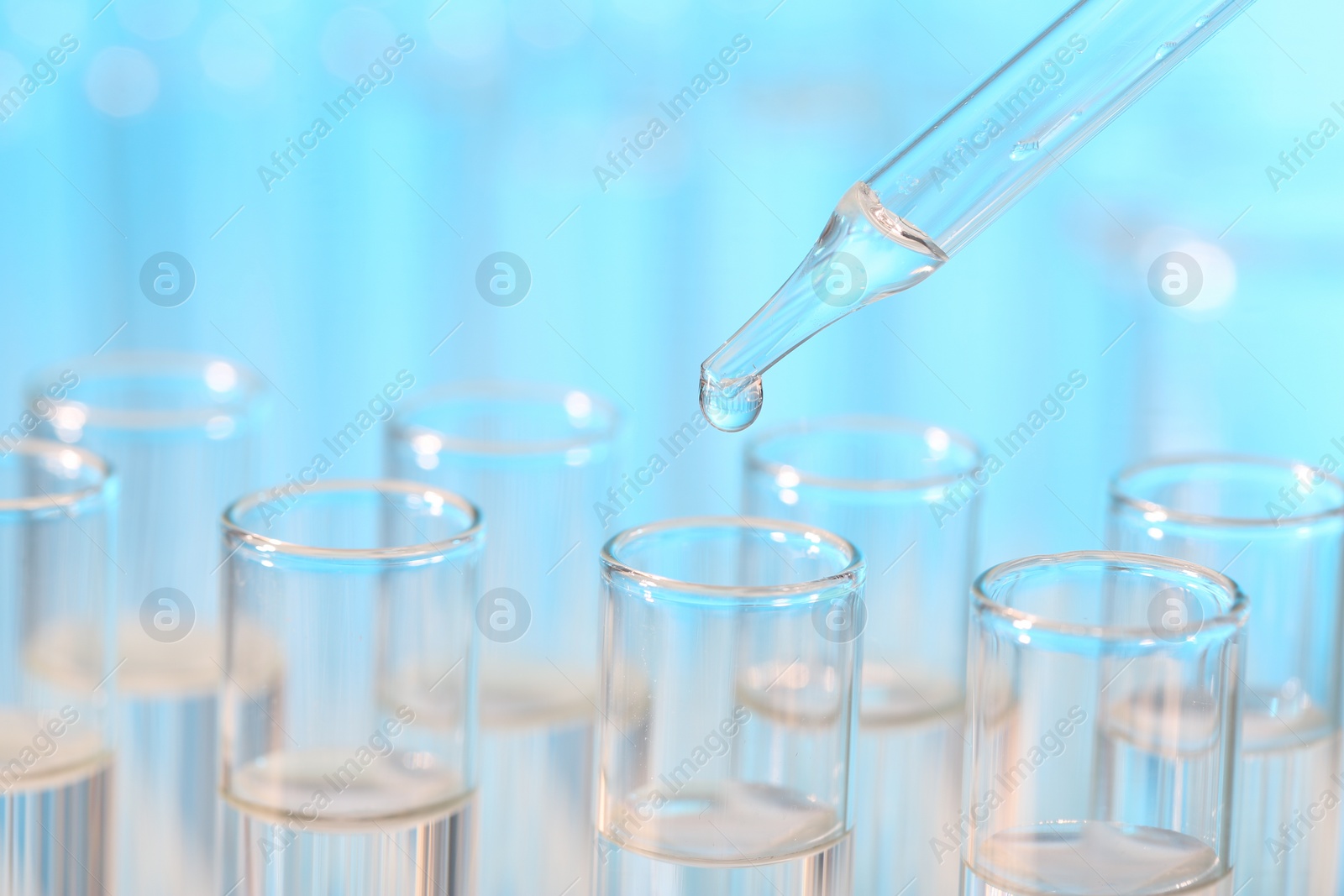 Photo of Laboratory analysis. Dripping liquid from pipette into glass test tube on light blue background, closeup