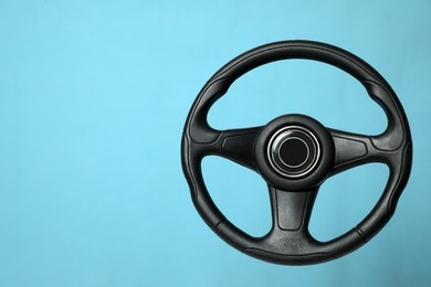 Photo of New black steering wheel on light blue background, space for text