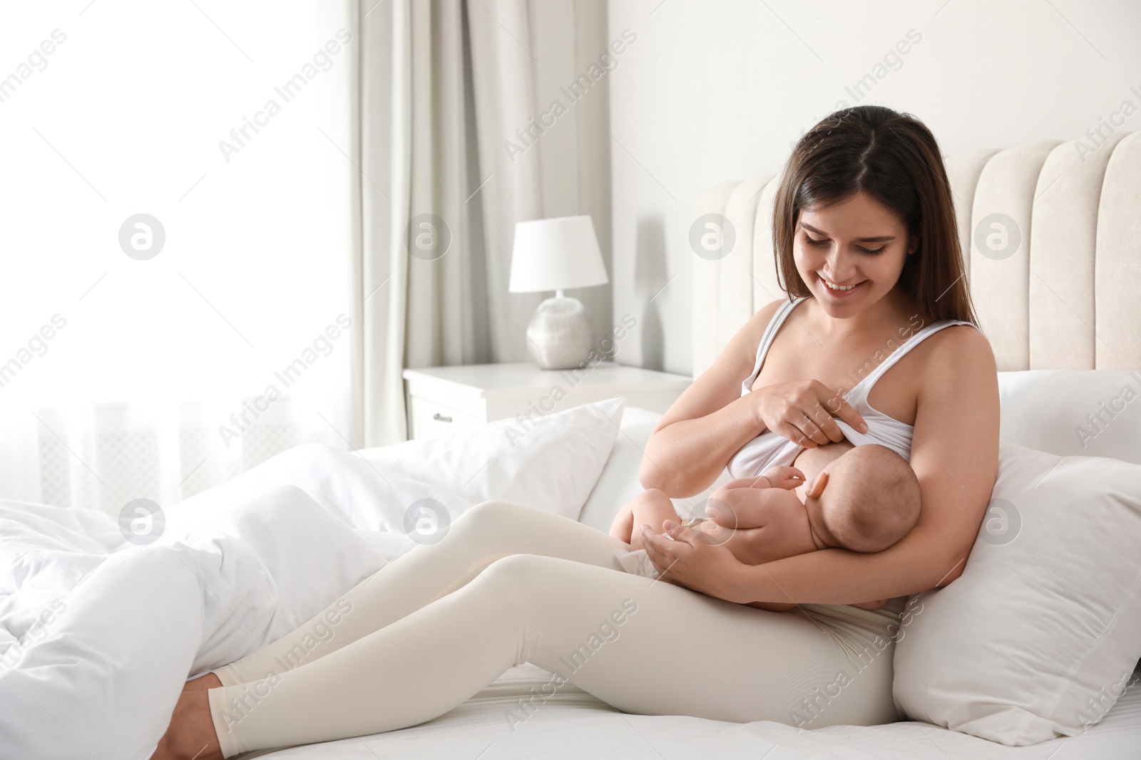 Photo of Young woman breastfeeding her little baby on bed at home