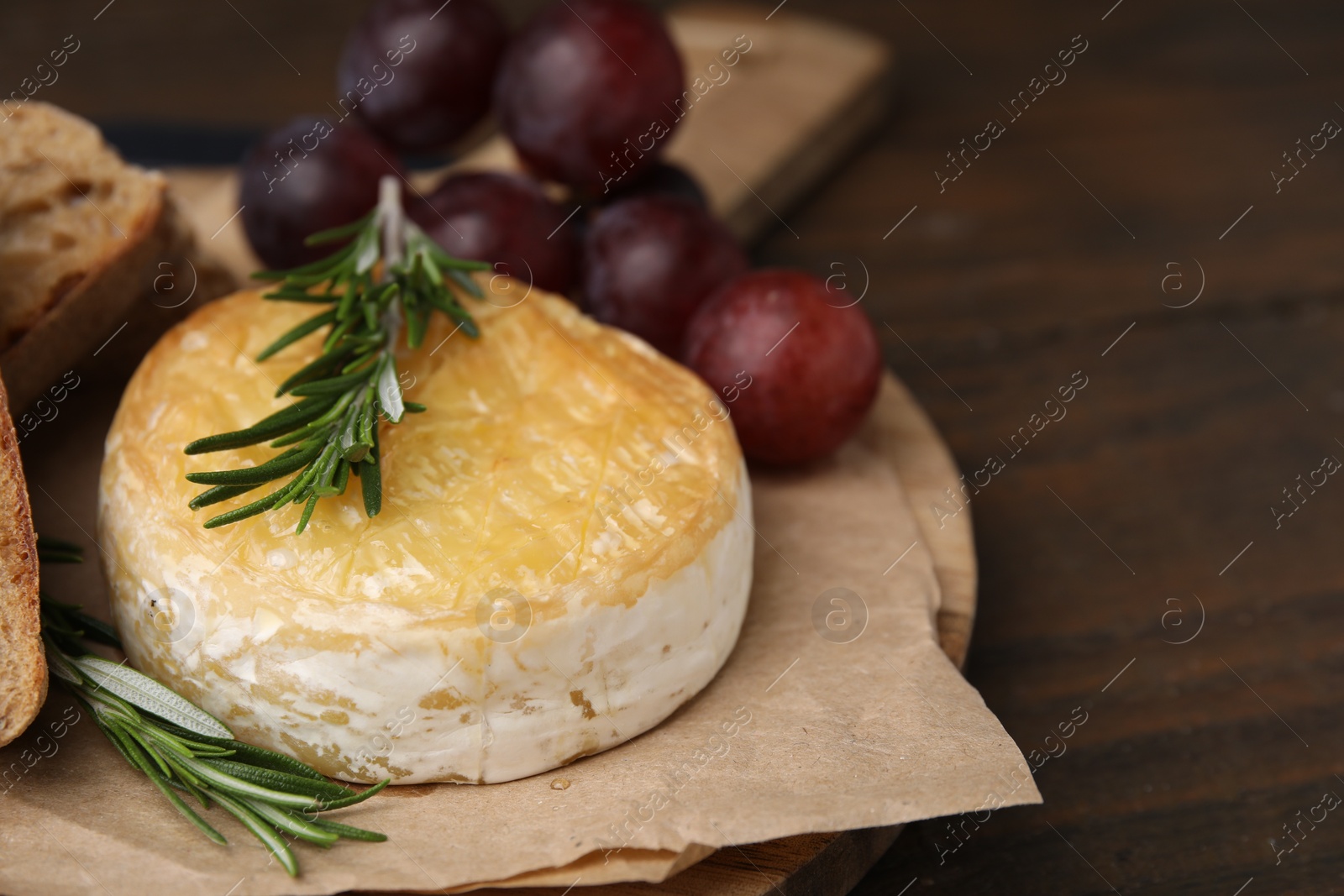 Photo of Tasty baked camembert, grapes and rosemary on wooden table, closeup. Space for text